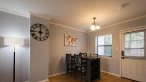 Un comedor con una mesa y sillas, un reloj de pared, una lámpara de pie y una ventana con persianas.