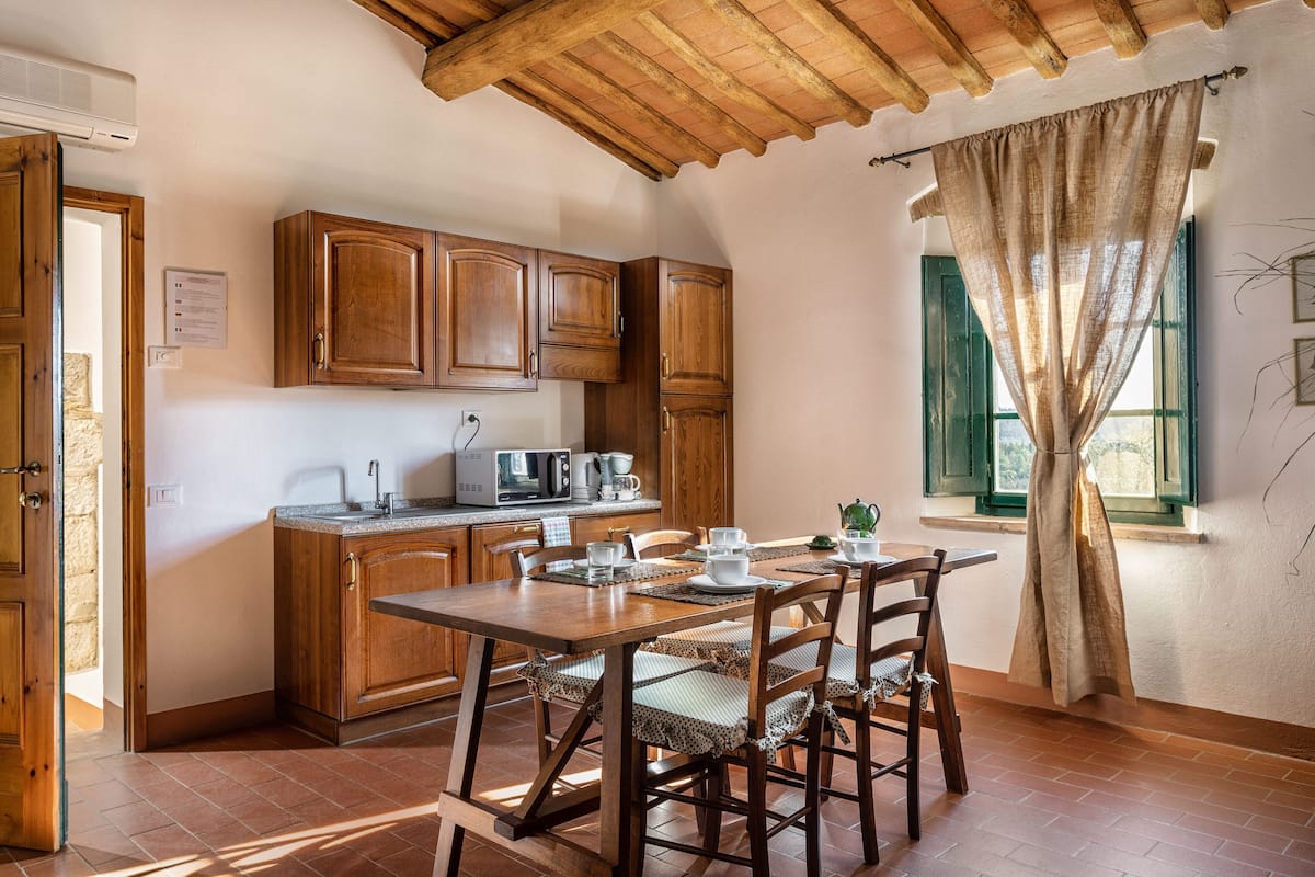 A kitchen with wooden cabinets, a dining table with chairs, and a window with curtains.
