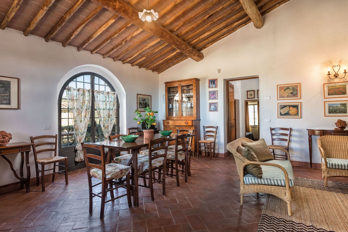 A dining area with wooden furniture, a large arched window, and a rustic ceiling.