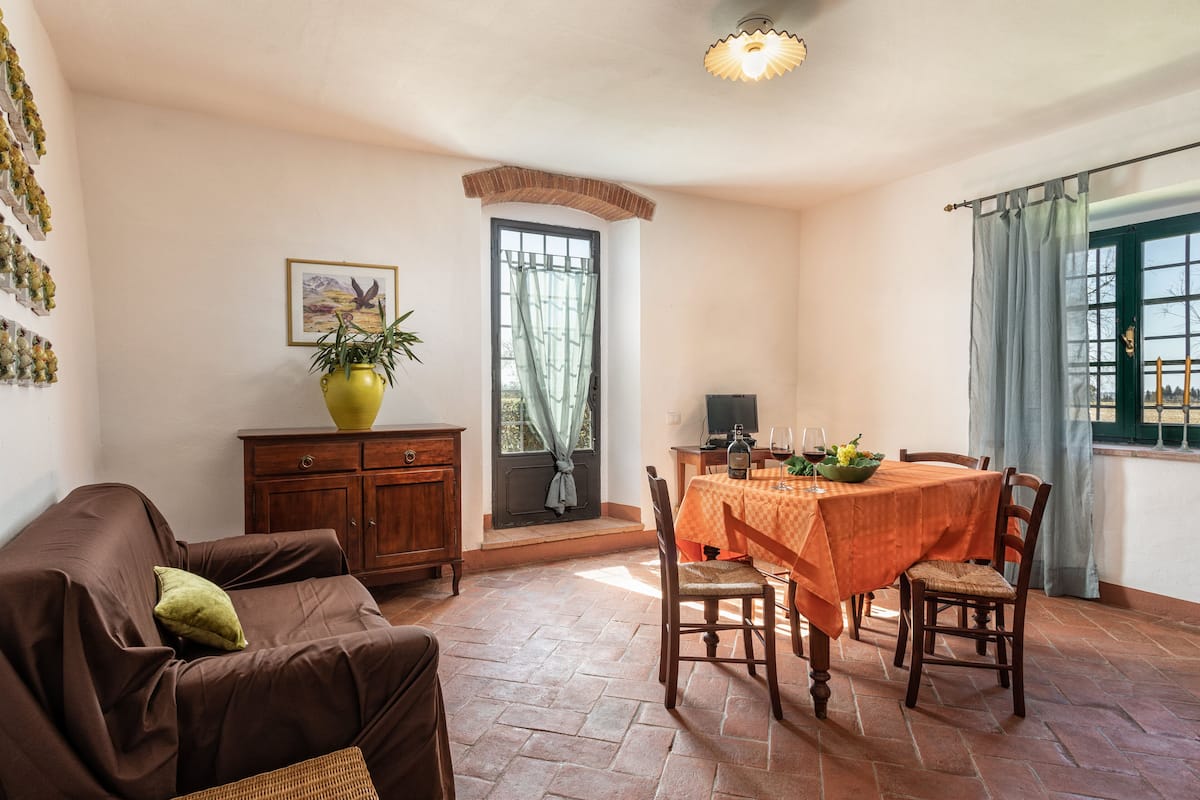 A cozy living room with a brown sofa, a dining table with an orange tablecloth, and a wooden cabinet.