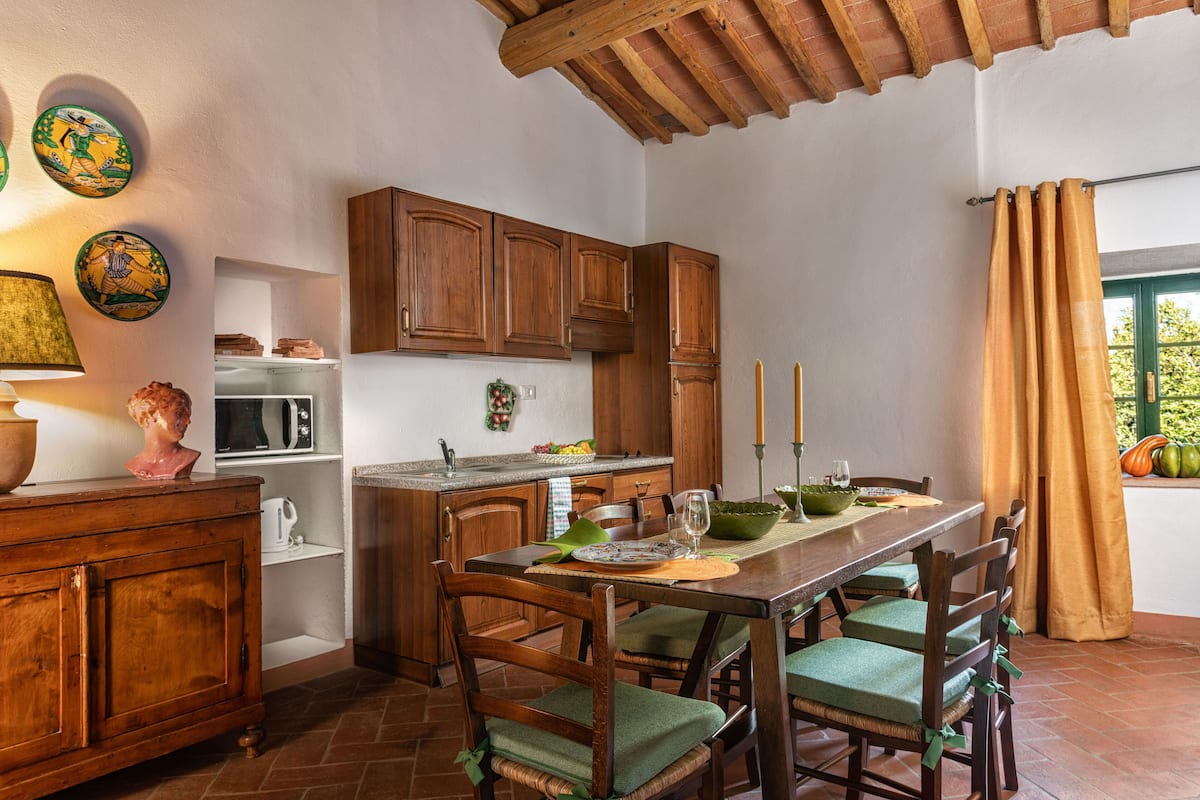 A kitchen with wooden cabinets, a dining table with chairs, and a window with curtains.