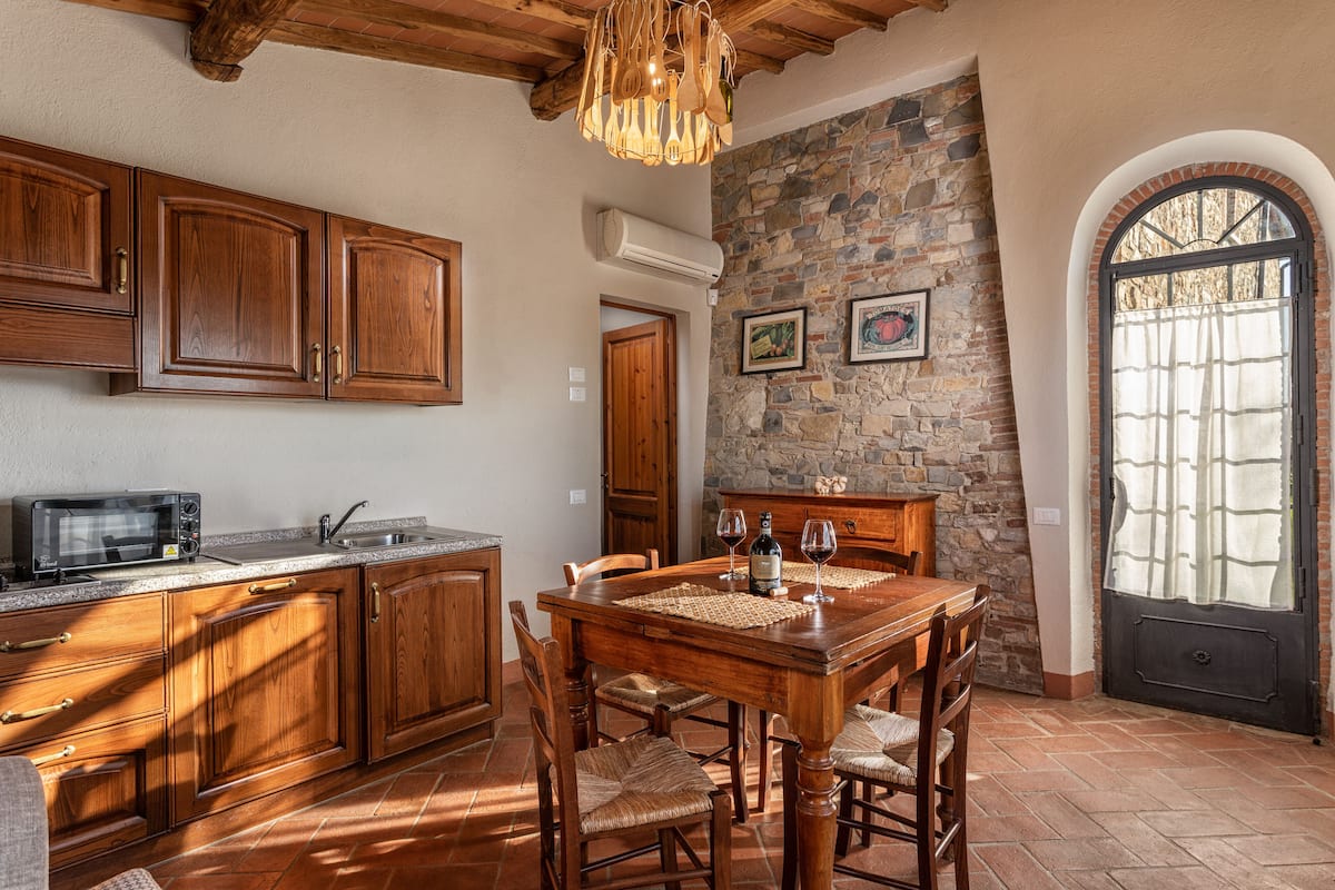 A kitchen with wooden cabinets, a stone wall, and a dining table with chairs.