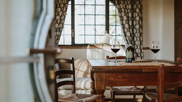 A dining table with two wine glasses and a bottle, surrounded by wicker chairs. - AGRITURISMO LA PAPESSA (Barberino Tavarnelle)