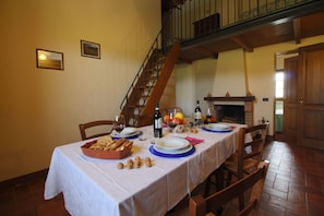 A dining table set with plates, glasses, and a bottle of wine, with a staircase and a fireplace in the background.