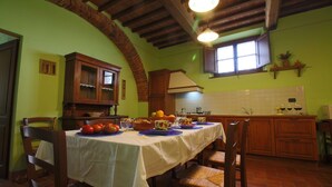 A dining area with a table set for four, surrounded by wooden chairs. A brick archway leads to another room.