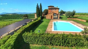 A villa with a swimming pool, surrounded by a well-maintained lawn and vineyard.