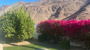 Una piscina con montañas al fondo, rodeada de césped verde y coloridas flores rosas.