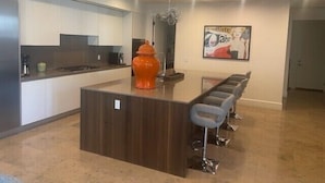 Una cocina moderna con una isla central, taburetes de bar y un jarrón naranja decorativo.