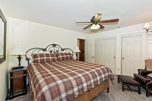 A bedroom with a bed, bedside lamps, a chair, a ceiling fan, and a door.