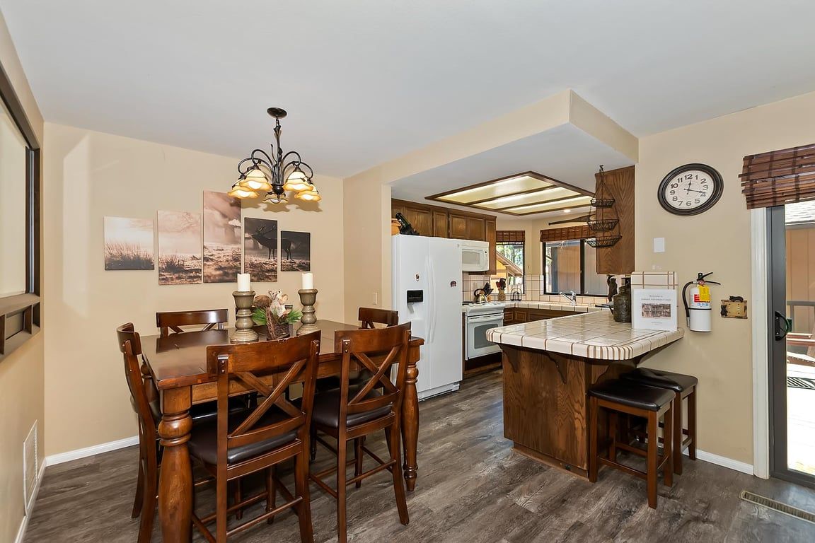 A kitchen with a dining area, wooden furniture, a white refrigerator, and a clock on the wall.