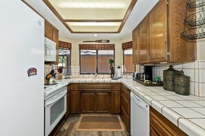A compact kitchen with wooden cabinets, a microwave, a stove, and a dishwasher. - Summit Adventure Condo by Destination Big Bear: Steps from Snow Summit Resort! Multiple Balconies! (Big Bear Lake)