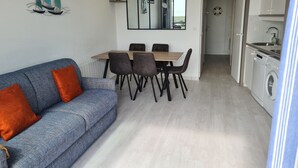 Ett kompakt bostadsutrymme med en soffa, ett matbord, stolar, en spegel och ett köksområde.