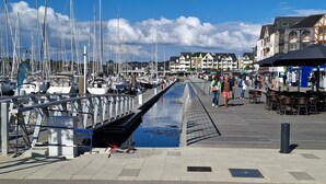 En småbåtshamn med förtöjda båtar, en gångväg för fotgängare och byggnader i bakgrunden.