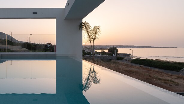 Ein moderner Poolbereich mit freiem Blick auf den Sonnenuntergang über dem Wasser.