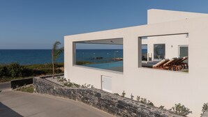 Ein modernes Gebäude mit einem großen Glasfenster, das einen Pool und das Meer überblickt.