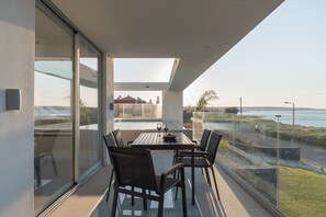 Un balcon moderne avec une table et des chaises en verre, donnant sur une zone côtière.