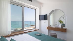 Ein Schlafzimmer mit großem Fenster, Flachbildfernseher, Nachttisch aus Holz und einer grünen Tagesdecke.