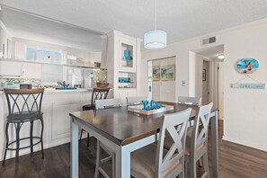 A modern kitchen with white cabinetry, a dining area with a wooden table and white chairs, and a view of the ocean through large windows.