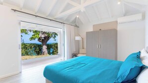 A bedroom with a large bed, a wardrobe, and a view of the sea through a glass door. - Le Caprice – Iconic Clifftop Estate Above Baie Rouge, Terres Basses (Lowlands)