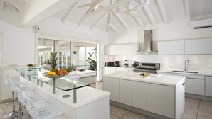 A modern kitchen with white cabinetry, a glass island with bar stools, and a large window providing natural light. - Villa Encore | A Grand Caribbean Estate with Panoramic Sea Views (Philipsburg)