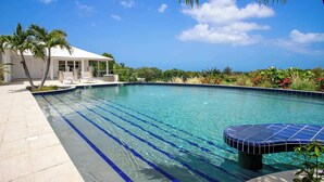 A clear blue swimming pool with a tiled edge, surrounded by a patio area with lounge chairs and a covered seating area. - Villa Encore | A Grand Caribbean Estate with Panoramic Sea Views (Philipsburg)