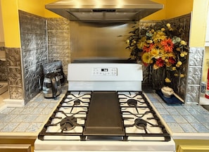 Une cuisine Ă©quipĂ©e dâune cuisiniĂšre Ă gaz, dâune machine Ă cafĂ© et dâun vase dĂ©coratif avec des fleurs.