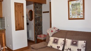 A cozy living room with a brown sofa, patterned cushions, a stone fireplace, wooden doors, and a framed picture on the wall.