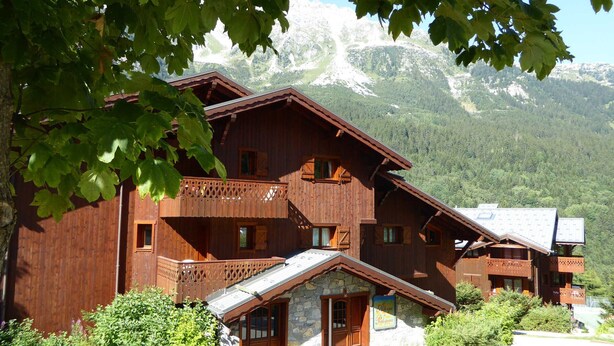 A wooden chalet with a stone entrance, balconies, and a mountain backdrop.