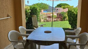 A patio with a table and chairs, a view of a garden, and a building in the background. - Cap Esterel le village T2 Garden level-CLIM-Sea view-Pool and parking included (Saint-Raphaël)