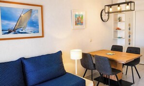 Een kamer met een houten eettafel, zwarte stoelen, een blauwe bank, een witte lamp, een schilderij van een zeilboot in een lijst, een klok en een plank met decoratieve objecten.
