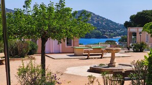 A courtyard with a fountain, benches, and a view of the sea and hills. - Cap Esterel le village T2 Garden level-CLIM-Sea view-Pool and parking included (Saint-Raphaël)