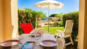 Un área de comedor al aire libre con una mesa preparada para dos personas, una silla roja y una blanca.