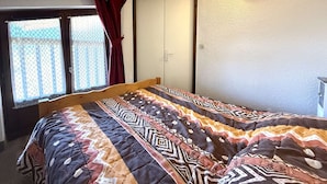 A bedroom with a bed, a window with curtains, a door, and a wall-mounted light fixture.