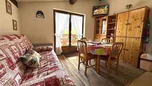 A cozy living room with a patterned sofa, a dining table set for four, and a wooden cabinet.