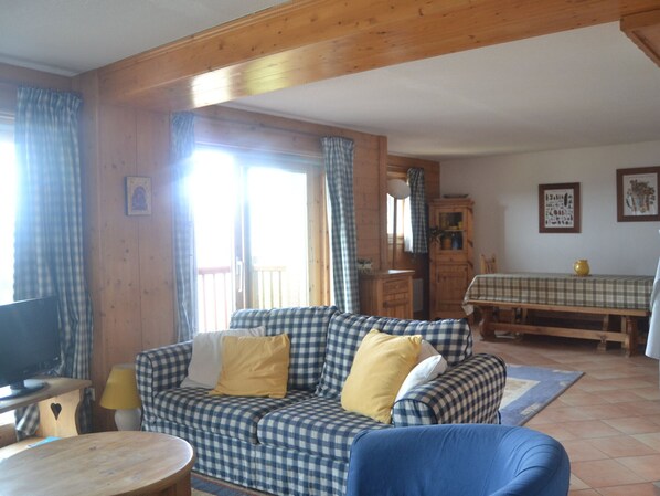 A cozy living room with a checkered sofa, a television, and a dining area with a table and chairs.