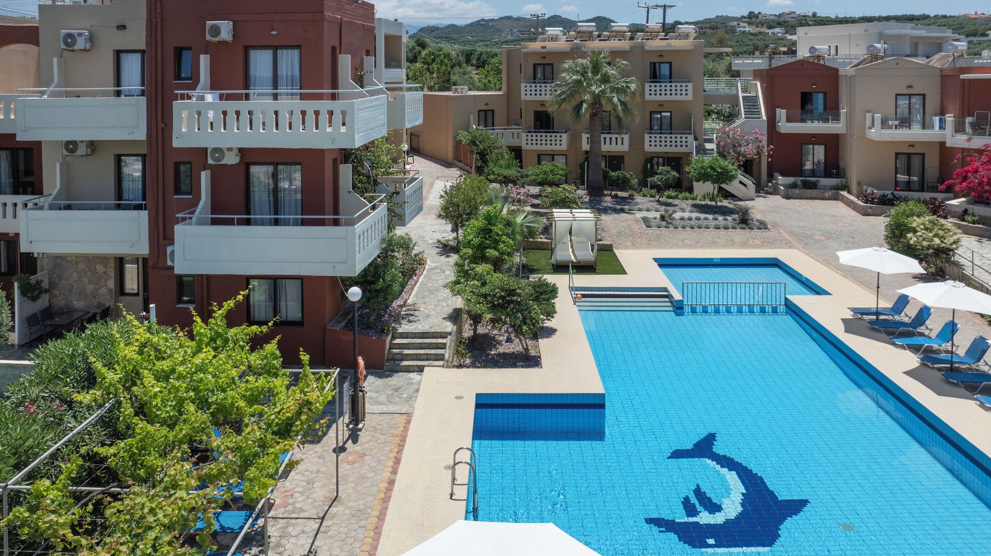 A swimming pool with a dolphin logo, surrounded by buildings with balconies and air conditioning units.