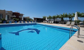 A swimming pool with a dolphin design, surrounded by lounge chairs and umbrellas, with buildings in the background. - Ekavi Apartments (Chania)