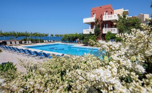 A swimming pool with lounge chairs, a red building with balconies, and a clear blue sky.
