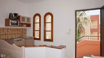 A compact kitchen with a microwave, coffee maker, and cabinets. There are two windows and a view of a building outside.