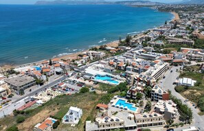 An aerial view of a coastal residential area with buildings, a swimming pool, and a beach. - Ekavi Apartments (Chania)