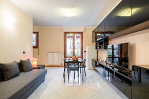 A modern living room with a sofa, dining table, chairs, a TV, and a large window.