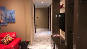 Een hotel lobby met een rode bank, een kleine tafel met een telefoon, een wandtelevisie en een gang naar andere kamers.