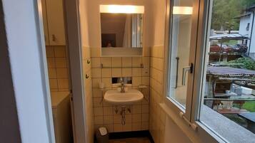 A narrow bathroom with a sink, mirror, and window.