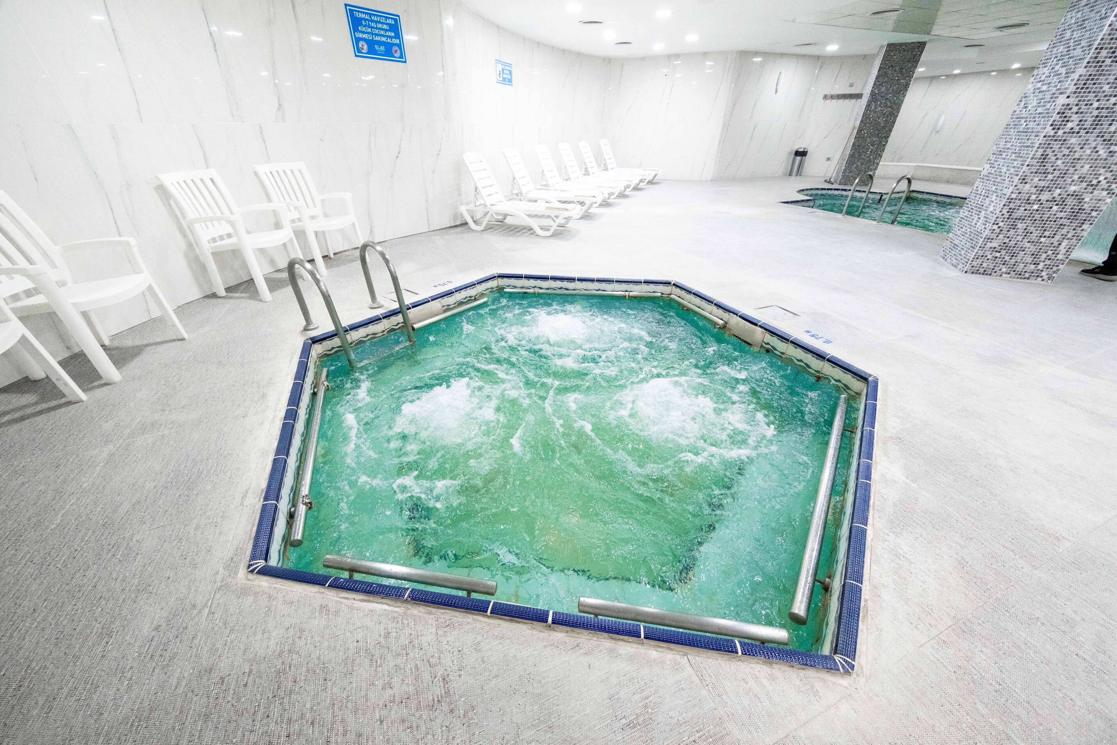An indoor swimming pool with a tiled border, surrounded by white lounge chairs.