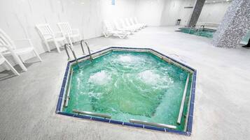 An indoor swimming pool with a tiled border, surrounded by white lounge chairs.