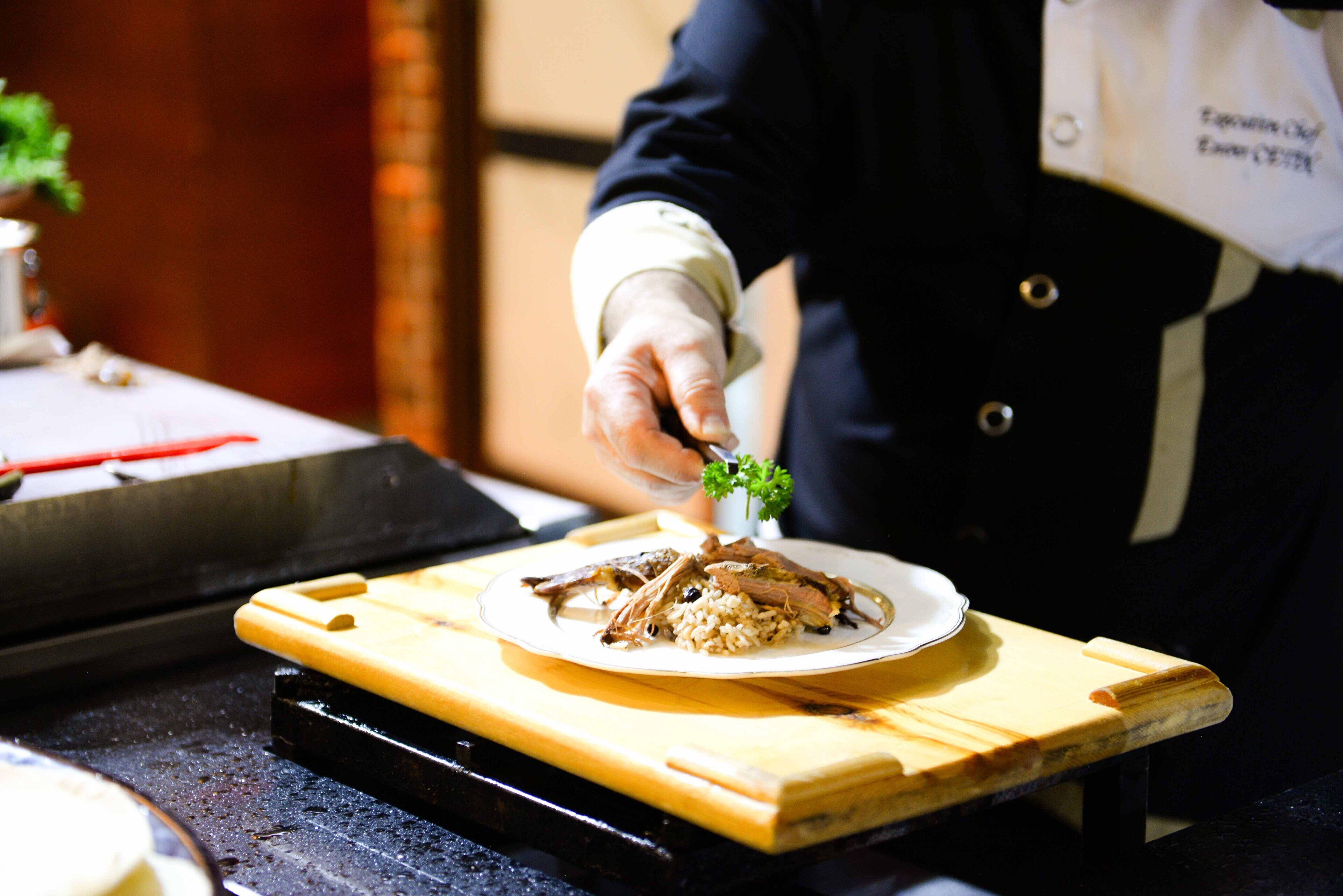 A chef placing a garnish on a plate of food.