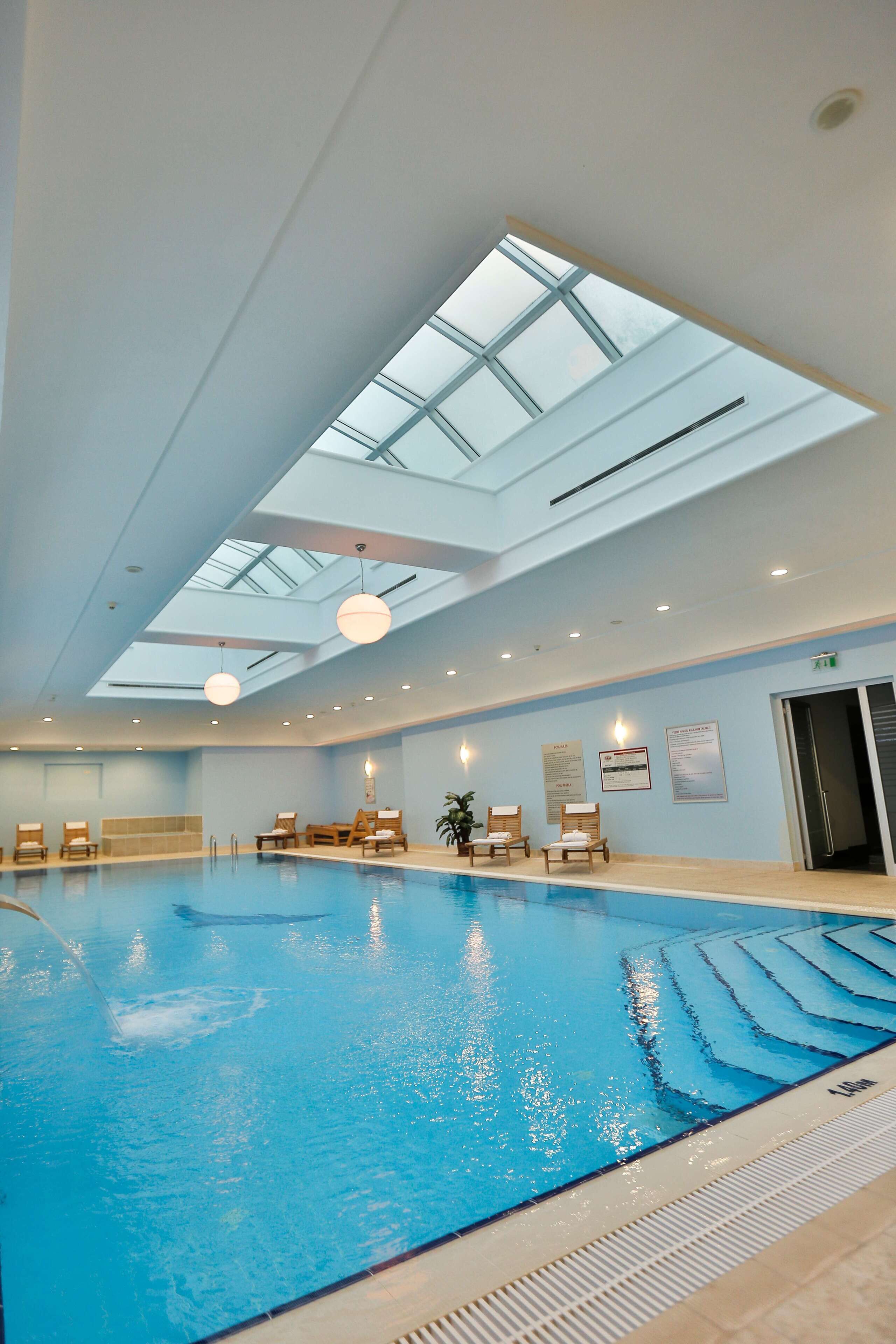 Une piscine intérieure dotée d’une verrière, de chaises longues et d’un plafond avec des spots encastrés.