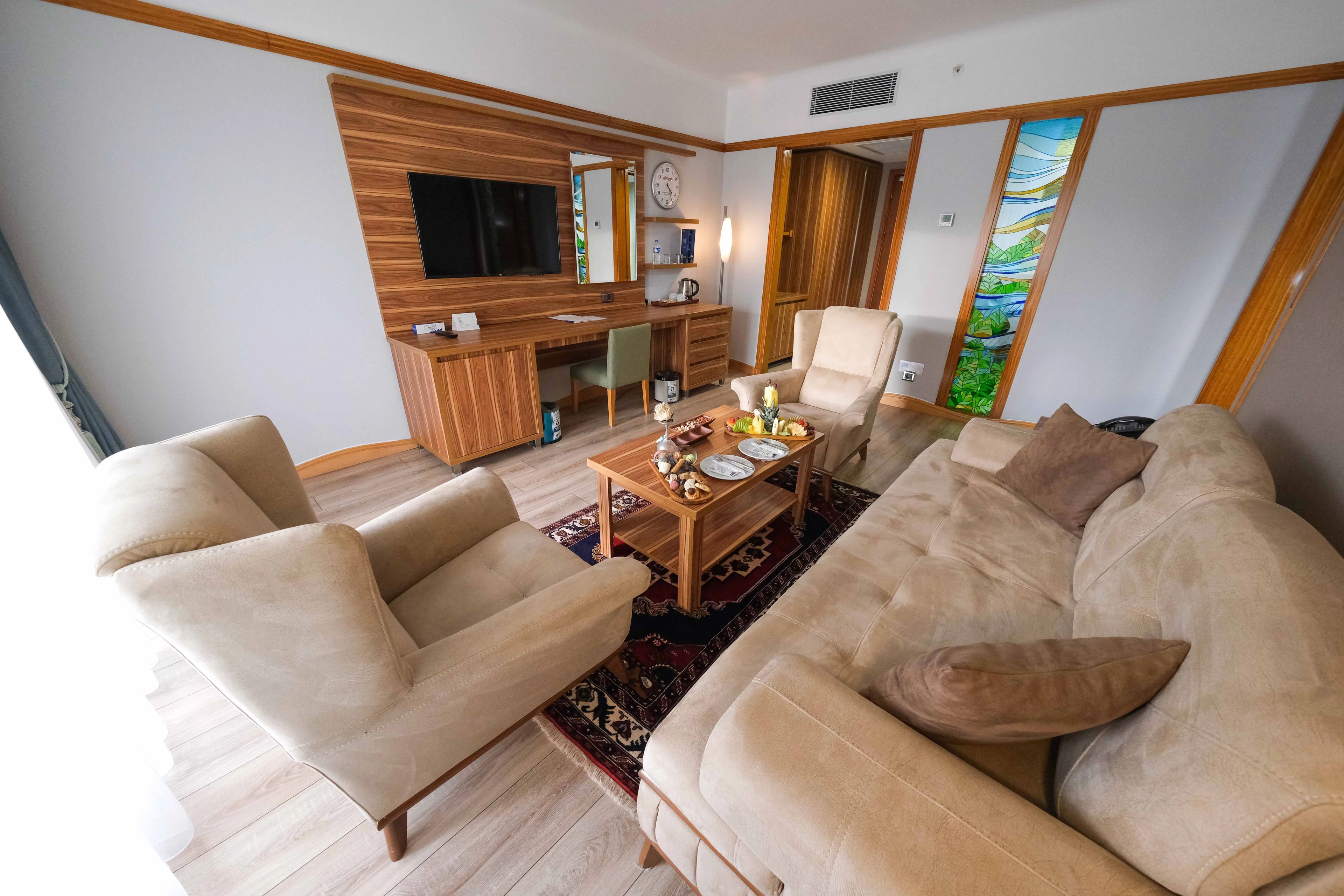 A living room with a sofa, armchairs, a coffee table with fruits, a TV, and a wooden cabinet.