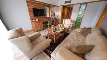 A living room with a sofa, armchairs, a coffee table with fruits, a TV, and a wooden cabinet.