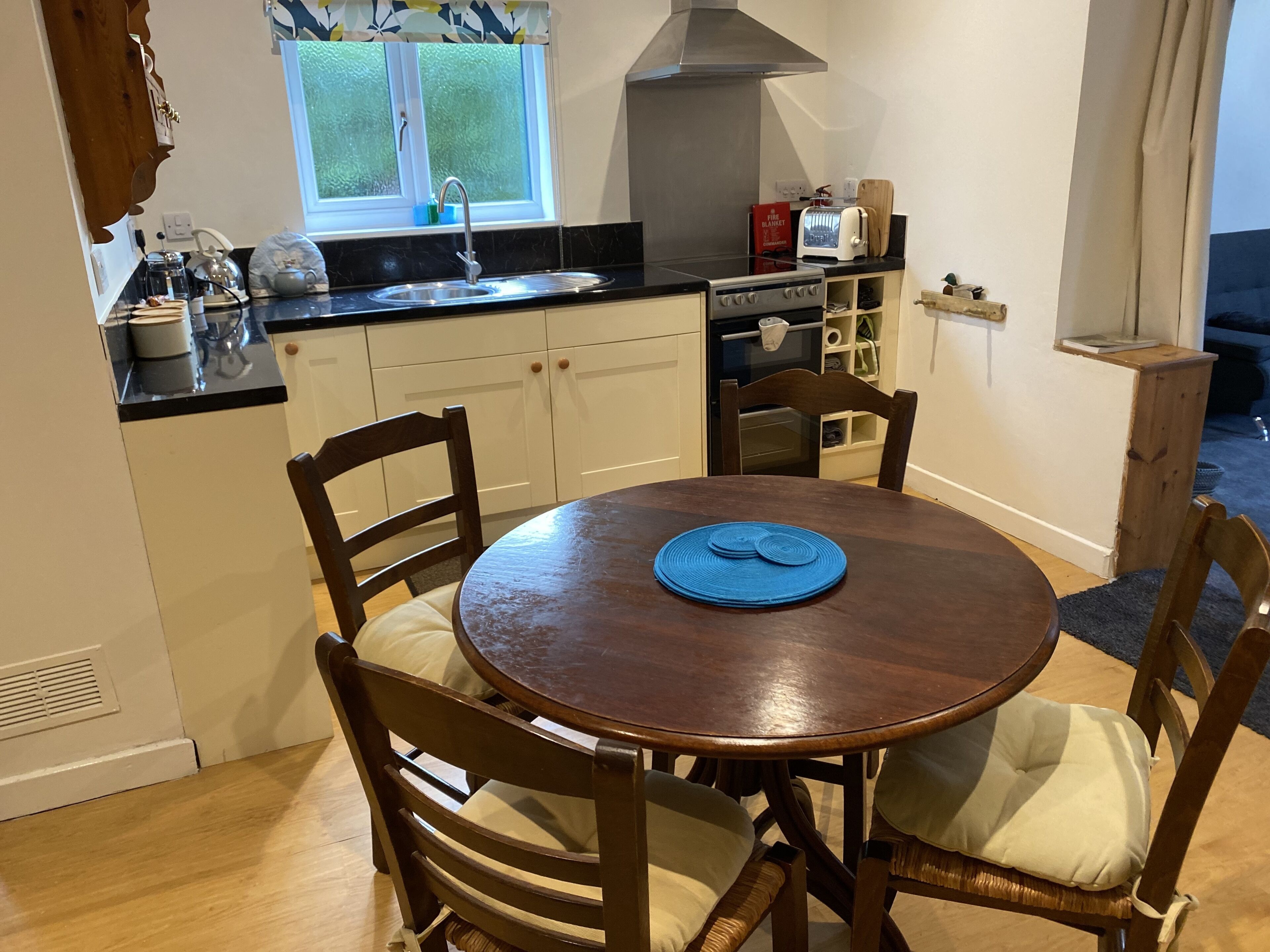 Een kleine keuken met een ronde eettafel, houten stoelen, een inbouwoven en een raam met uitzicht.